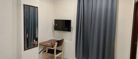 A small room with a desk, chair, a mounted TV, and a window with curtains.