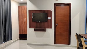 Ein Zimmer mit Holztür, einem an der Wand befestigten Fernseher, einem kleinen Tisch und einem Stuhl.