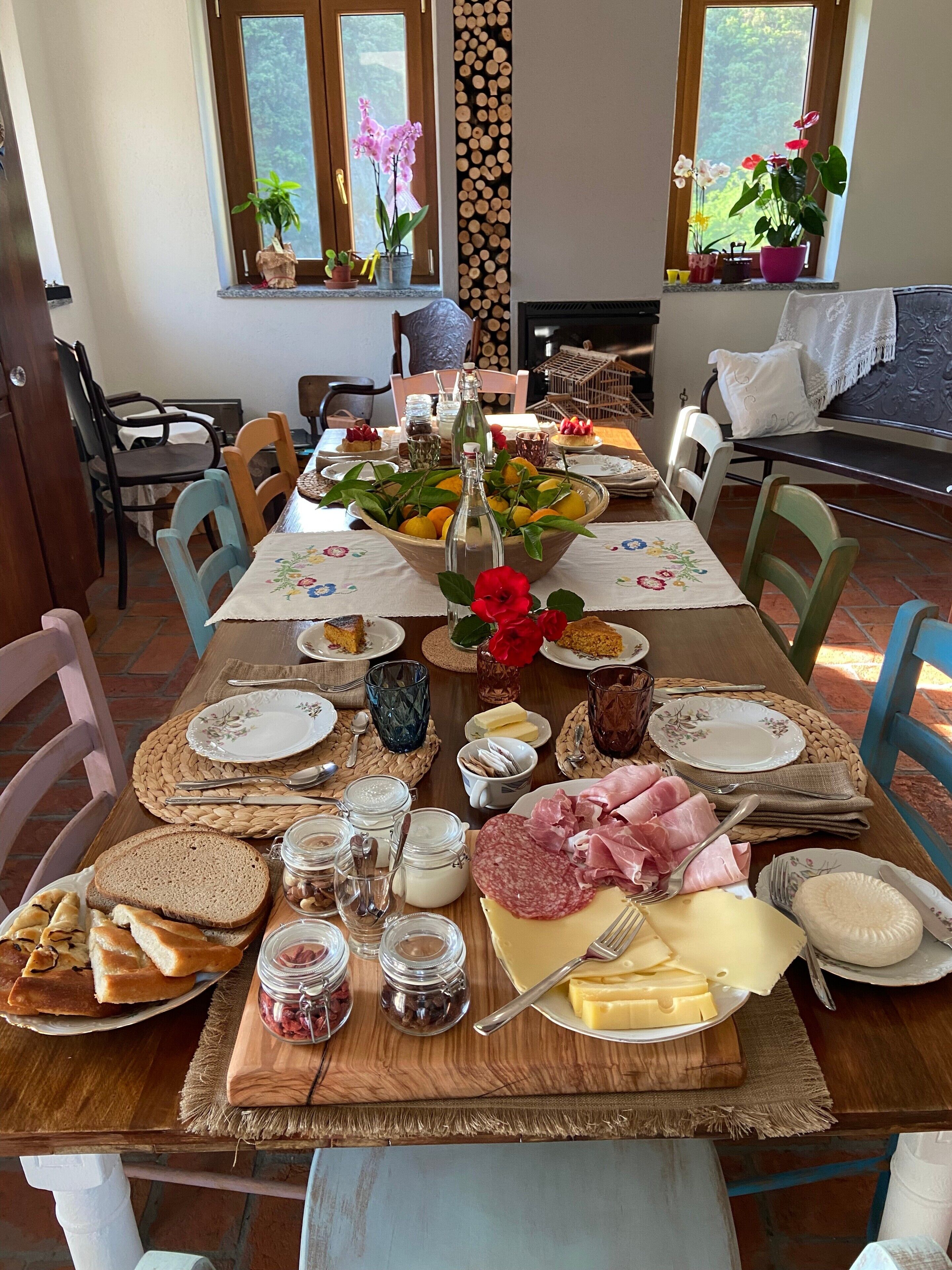 Una mesa de comedor dispuesta con diversos alimentos y bebidas, rodeada de sillas y vista al exterior.