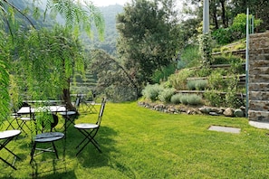 Un espace extérieur verdoyant, avec des tables et des chaises, entouré d’arbres et d’un mur de pierre.