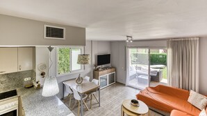 Een moderne woonkamer met een bank, een eettafel en een keukenhoek, inclusief een televisie en kastjes.