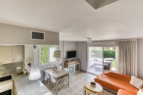 A modern living room with a sofa, a dining table, and a kitchen area with a TV and cabinets.