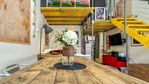 Una mesa de madera con un jarrón de flores, un mapa en la pared y una escalera amarilla.