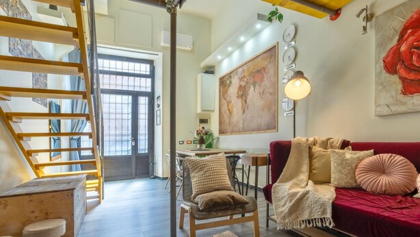 Una sala de estar acogedora con un sofá rojo, una mesa de centro de madera y una escalera que lleva a un nivel superior.