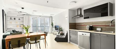 Una cocina moderna con lavavajillas, un comedor con mesa y sillas, y una sala de estar con sofá y televisor.