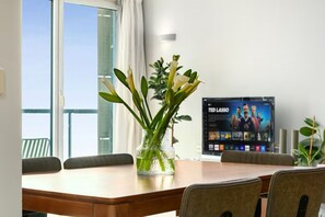A conference room with a wooden table, chairs, a vase with green plants, a poster on the wall, and a window with curtains.
