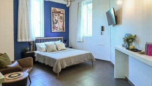 A bedroom with a bed, a desk, a chair, a TV, and artwork on the wall.