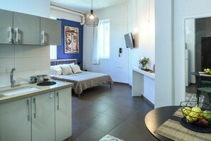 Ein kompakter Wohnraum mit Küchenzeile, einem Bett mit Kopfteil, einem Essbereich und einem an der Wand montierten Fernseher.