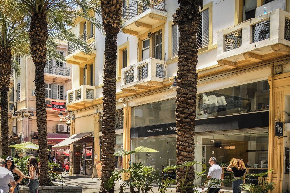 A building with multiple balconies, palm trees, and storefronts with signage.