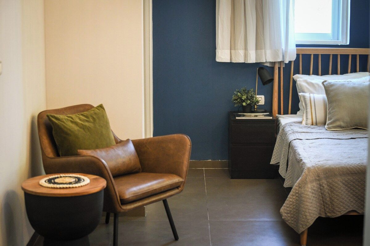 A bedroom with a bed, a chair, a nightstand, and a window with curtains.