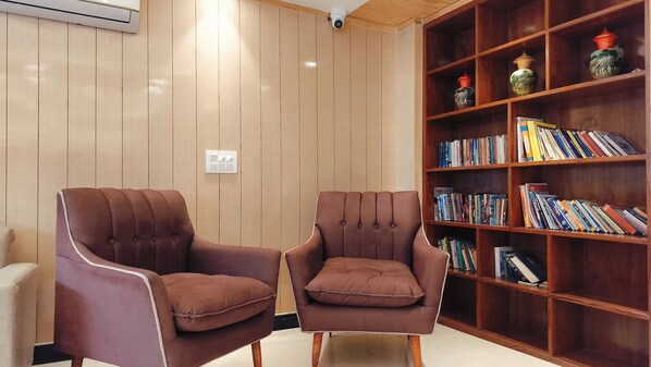 A room with two brown armchairs, a wooden bookshelf filled with books, and a white air conditioning unit on the wall. - Hotel Highland Bhagsu (Dharamshala)
