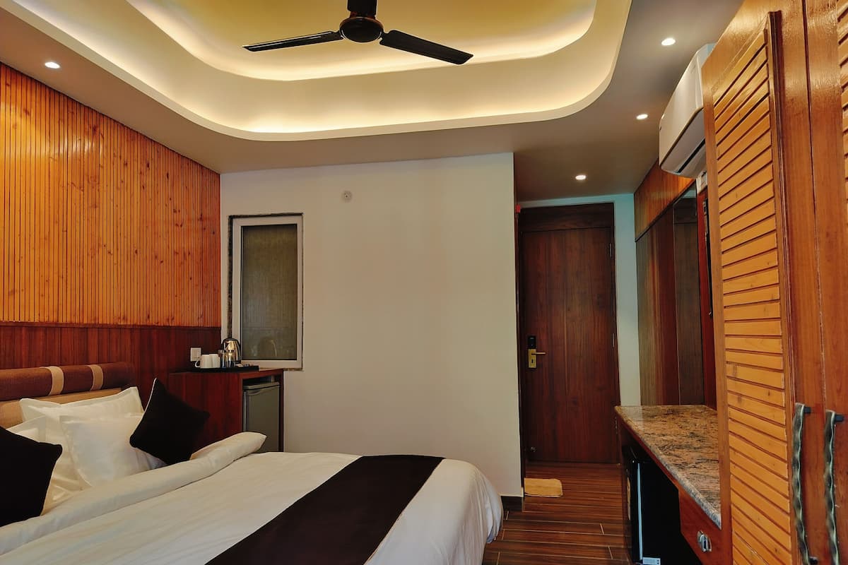 A modern hotel room with a large bed, wooden paneling, a ceiling fan, and a small kitchenette.