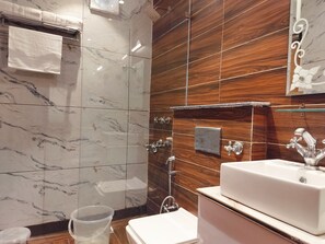 A bathroom with a marble wall, wooden paneling, a white sink, and a shower with a handheld showerhead. - Hotel Highland Bhagsu (Dharamshala)