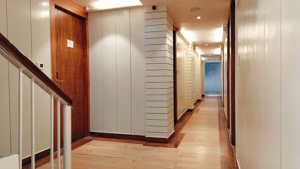 Un couloir doté d’un plancher en bois, de murs blancs et d’une porte en bois portant un numéro.