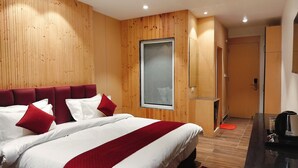 Habitación de hotel con una cama grande, paneles de madera, un ventanal y una puerta que da a un baño.