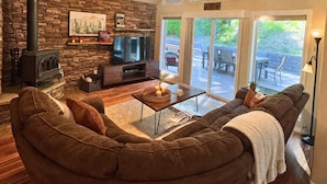 Una sala de estar acogedora con chimenea de piedra, televisor y ventana grande con vistas a una terraza.