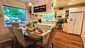 Una cocina moderna con armarios blancos, un comedor con mesa de madera y vistas a zonas verdes.
