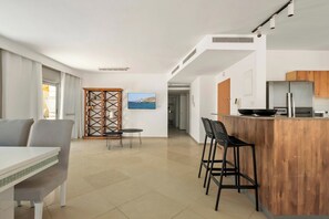 Cozinha moderna com ilha de madeira, área de refeições com mesa e cadeiras, e vista para o mar através de uma janela.