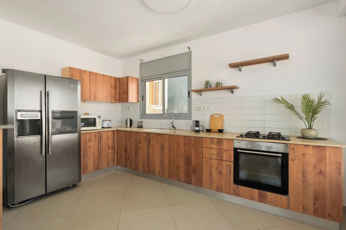 A modern kitchen with wooden cabinets, a stainless steel refrigerator, a microwave, a coffee maker, and a stove.