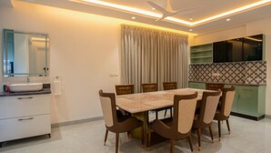 A modern dining area with a rectangular table and six chairs, a ceiling fan, and a kitchen with green cabinets and a tiled backsplash. - Let Home (Hyderabad)