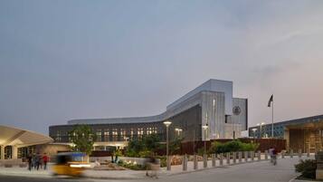 A modern building with a curved facade, a flagpole, and a landscaped area with trees and shrubs.