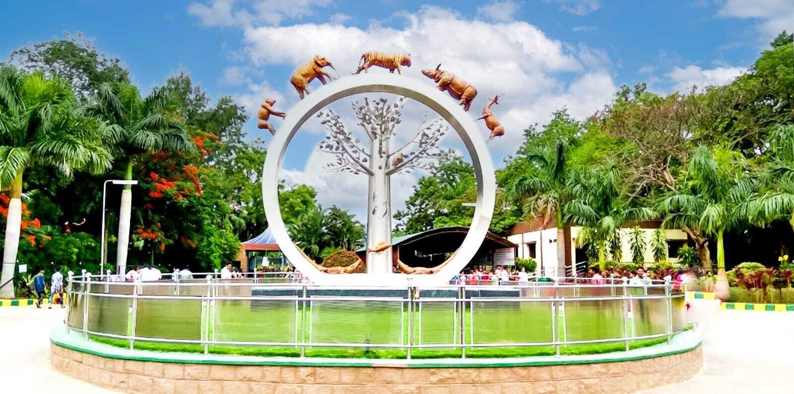 Una vasca d'acqua circolare con una scultura a forma di albero al centro, circondata da una ringhiera in metallo e un cordolo in pietra.