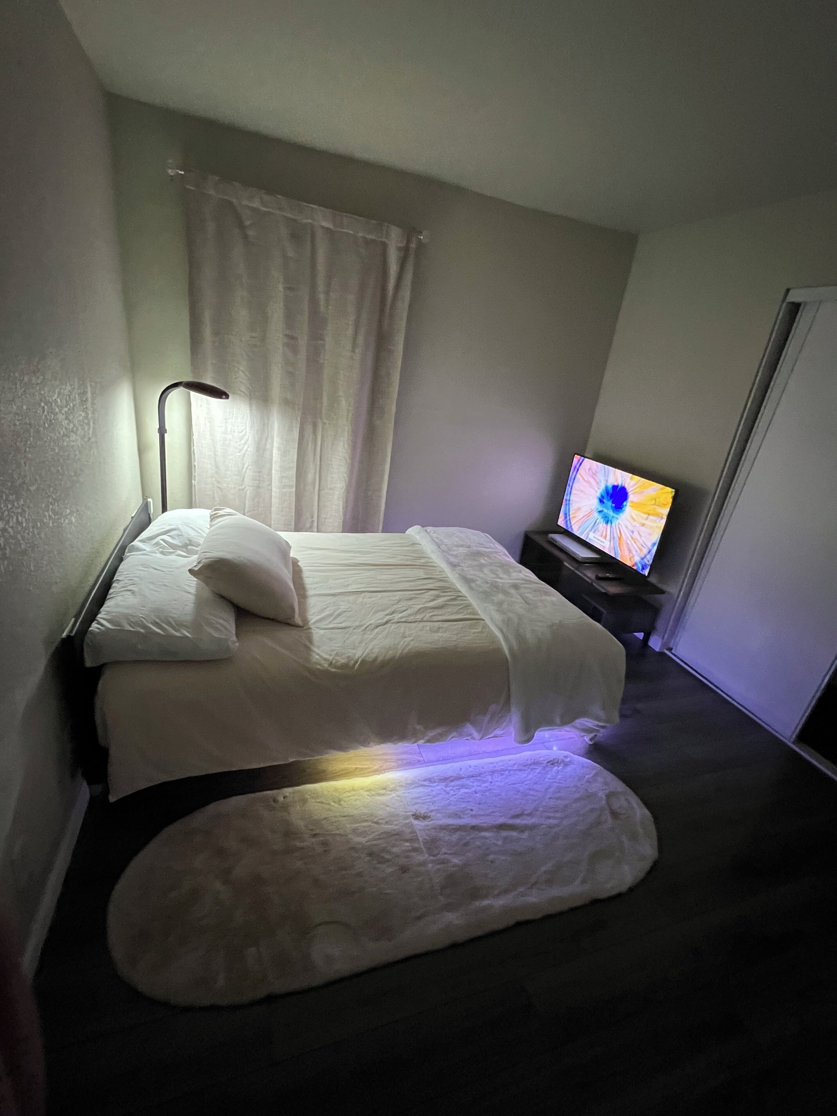 Een hotelkamer met een bed, een televisie, een lamp en een raam met gordijnen.