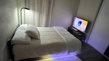 Een hotelkamer met een bed, een televisie, een lamp en een raam met gordijnen.