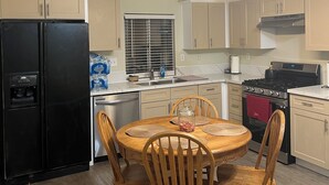 Una cocina con una mesa de comedor, sillas, un refrigerador, estufa y alacenas.