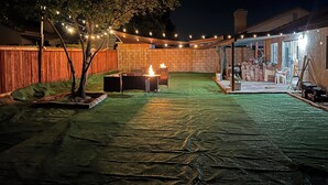 Un patio trasero con un pozo de fuego, luces colgantes y un área de porche techado.