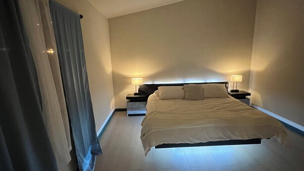 Un dormitorio moderno con cama, mesitas de noche y cortinas.