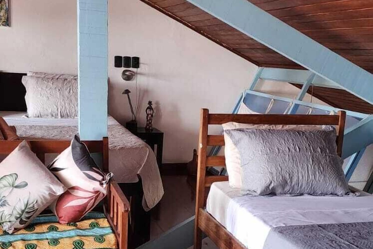 A cozy attic bedroom with two wooden bunk beds, a small bedside table with a lamp, and a white wall.