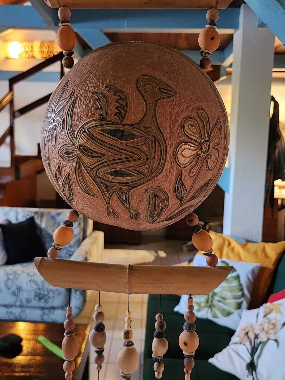 A wooden decorative item with a carved rooster and floral design, hanging from a structure with multiple wooden elements.