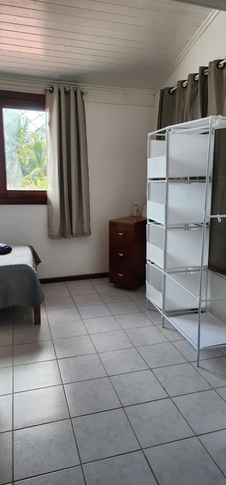A bedroom with a bed, a dresser, a window with curtains, and a white shelving unit.
