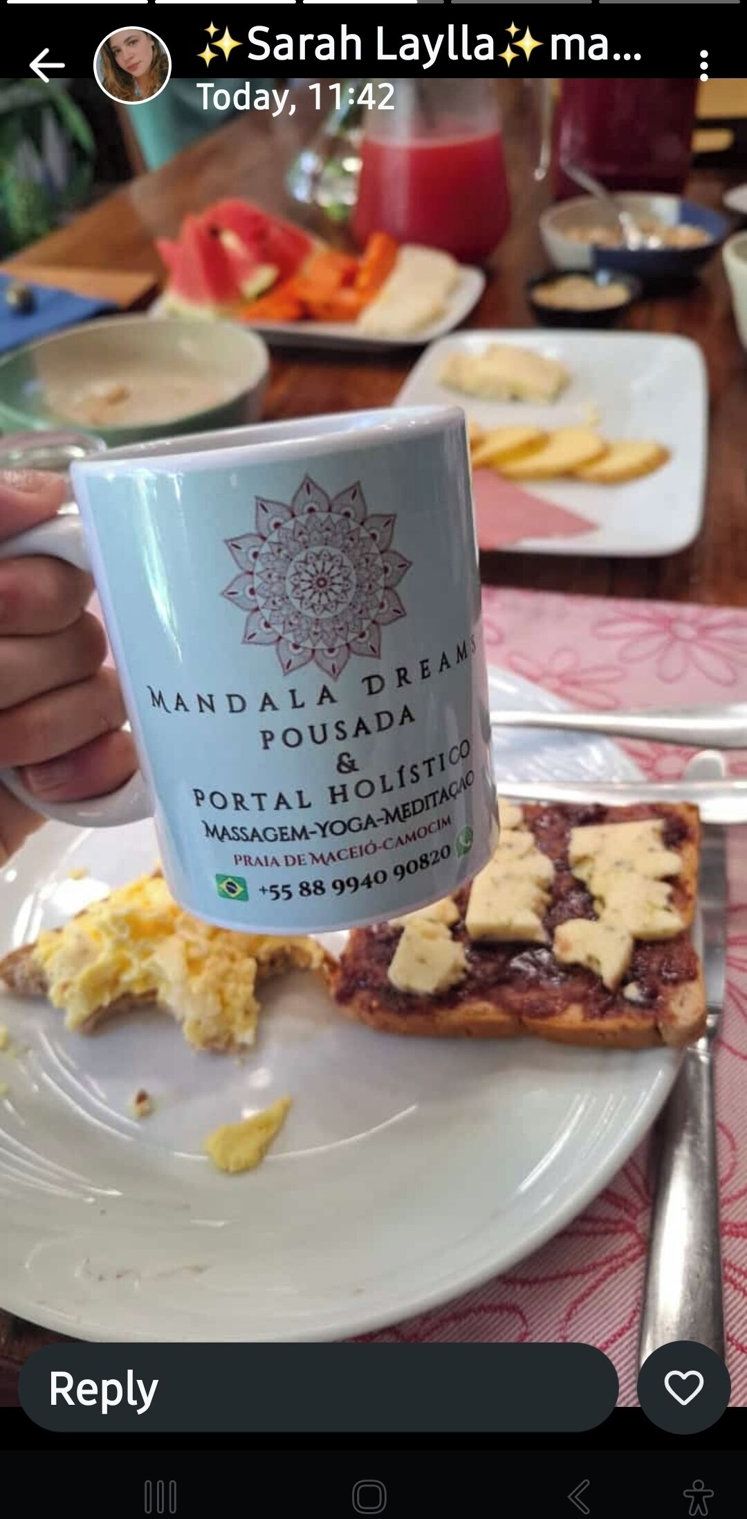 A person holding a mug with a mandala design and text, next to a plate with scrambled eggs and toast.