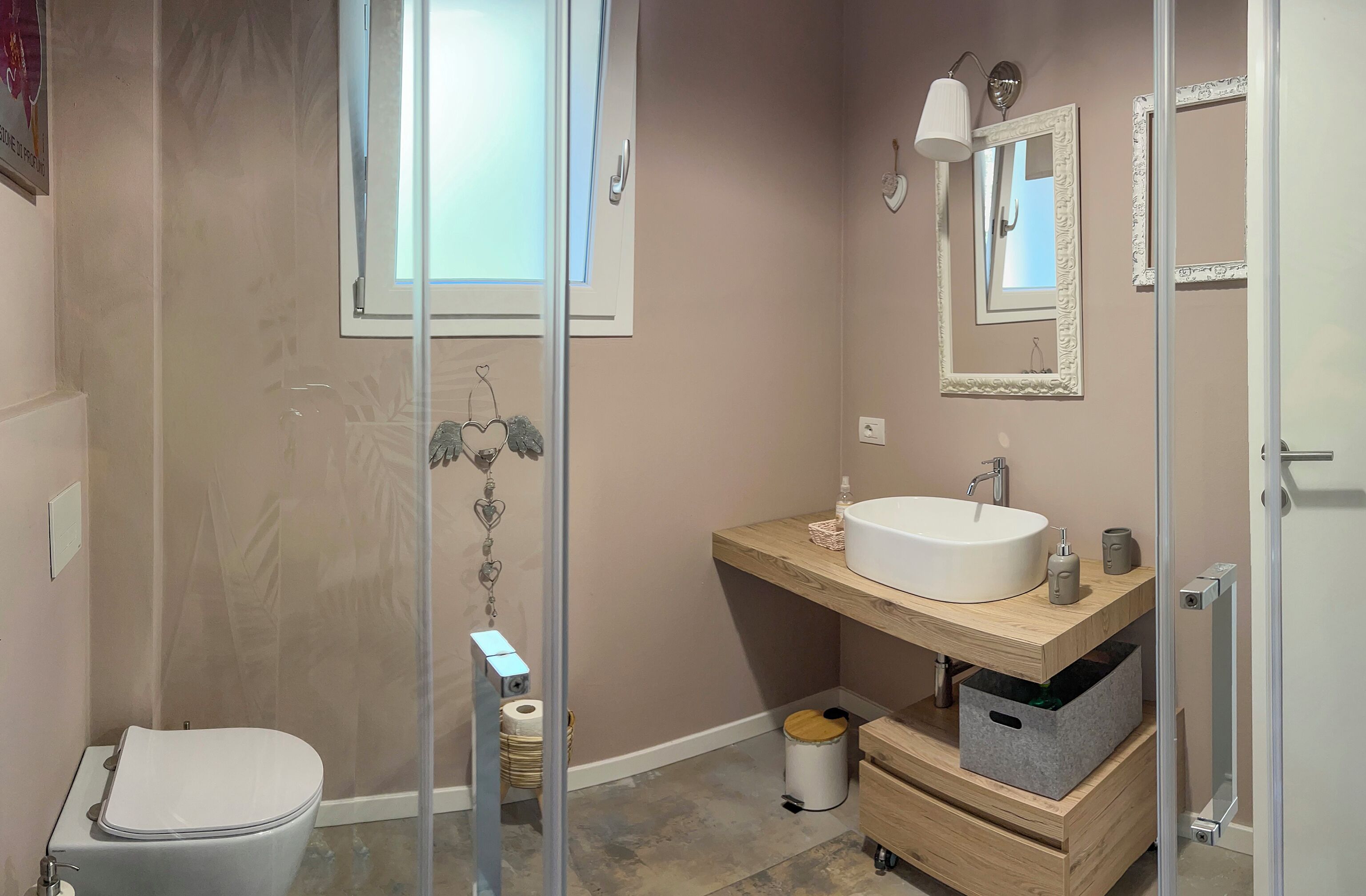 Et moderne badeværelse med en glasbrusekabine, et hvidt toilet og en trævasketøje med vask og spejl.