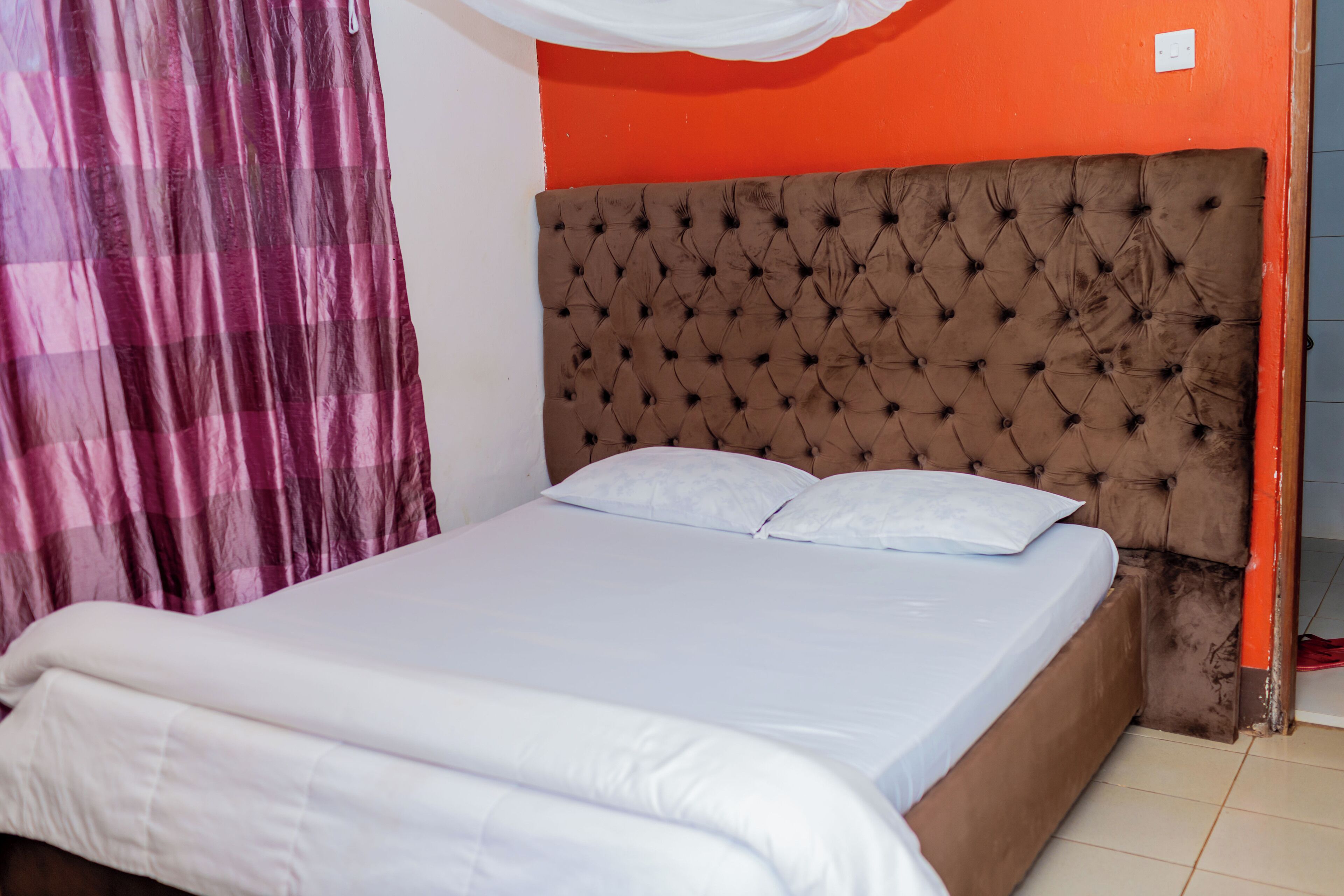A bed with a tufted headboard, white bedding, and a red wall.