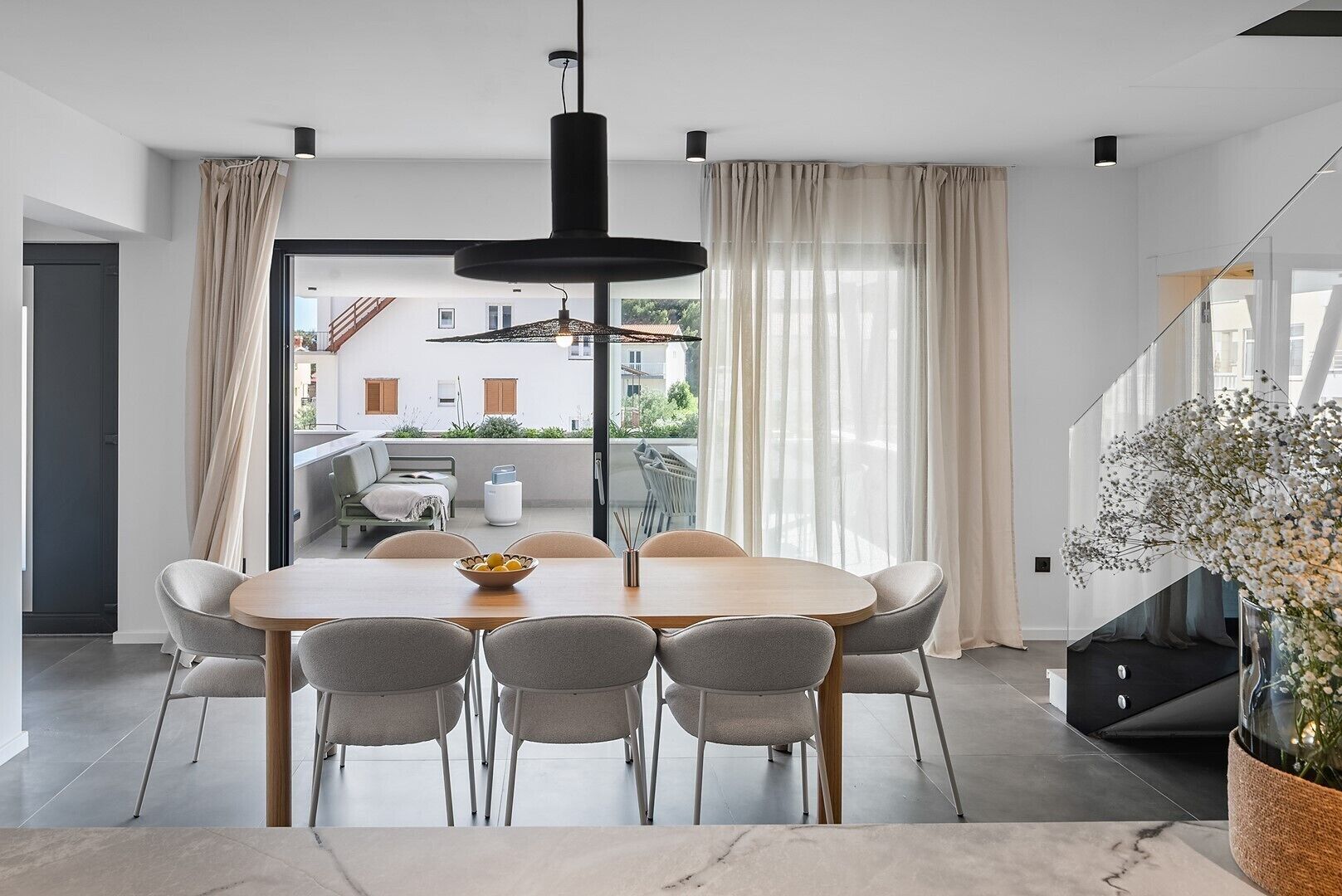 A modern dining area with a round table, six chairs, and a bowl of fruit.