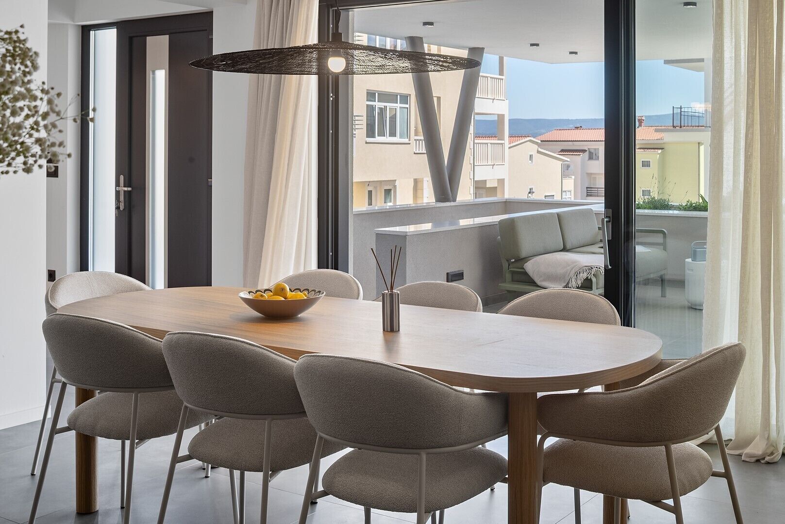 Un comedor moderno con una mesa de madera y seis sillas, un cuenco de limones y una lámpara colgante.