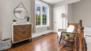 Una habitación con un armario de madera, un espejo redondo, una ventana con cortinas, una silla, una lámpara y una escalera de madera.