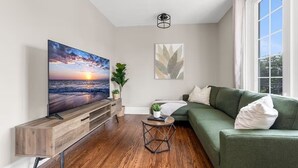 Una sala de estar moderna con un televisor de pantalla plana, un sofá verde, una mesa de centro y un mueble de televisión de madera.