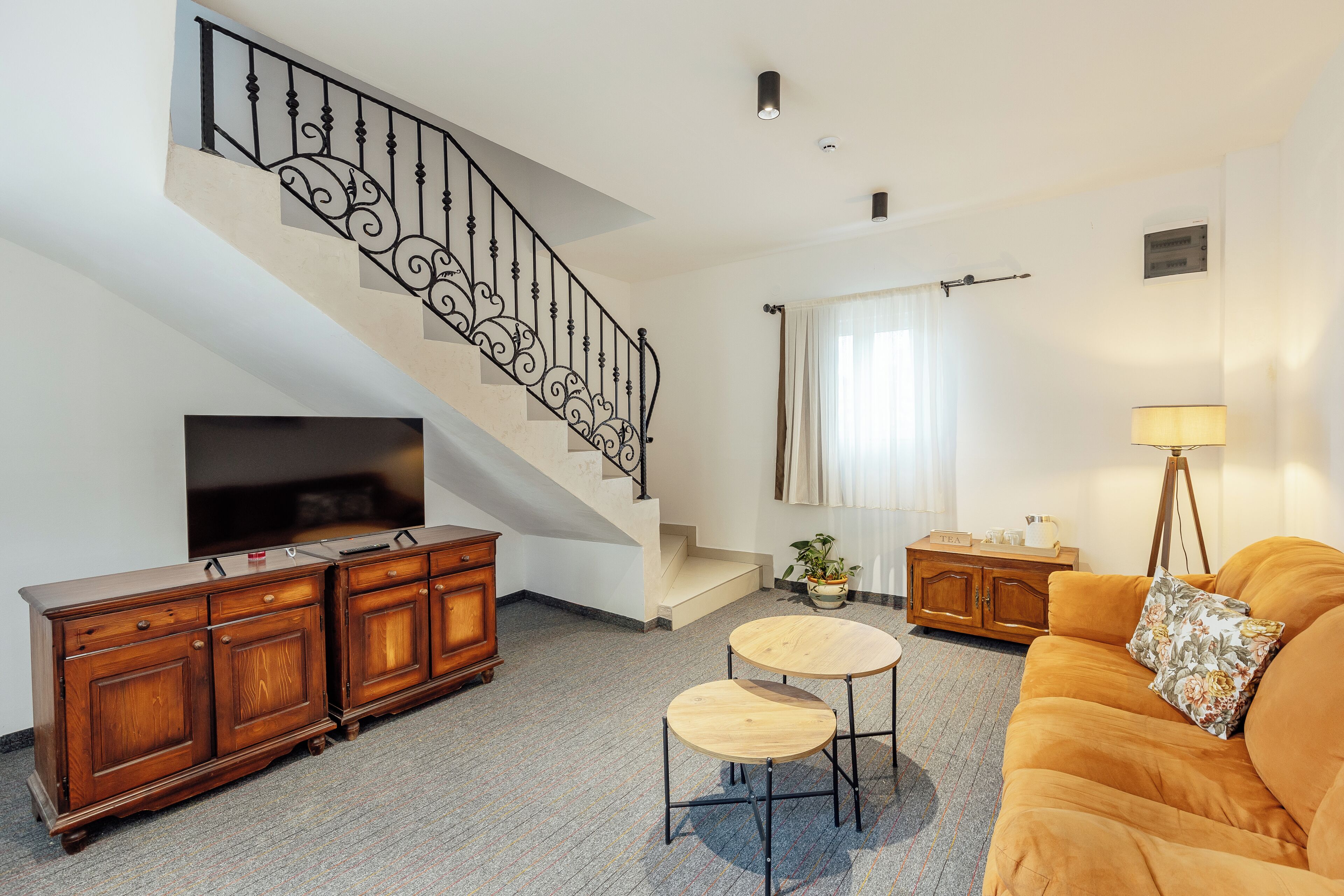 A living room with a staircase, a television, a sofa, a coffee table, and a lamp.
