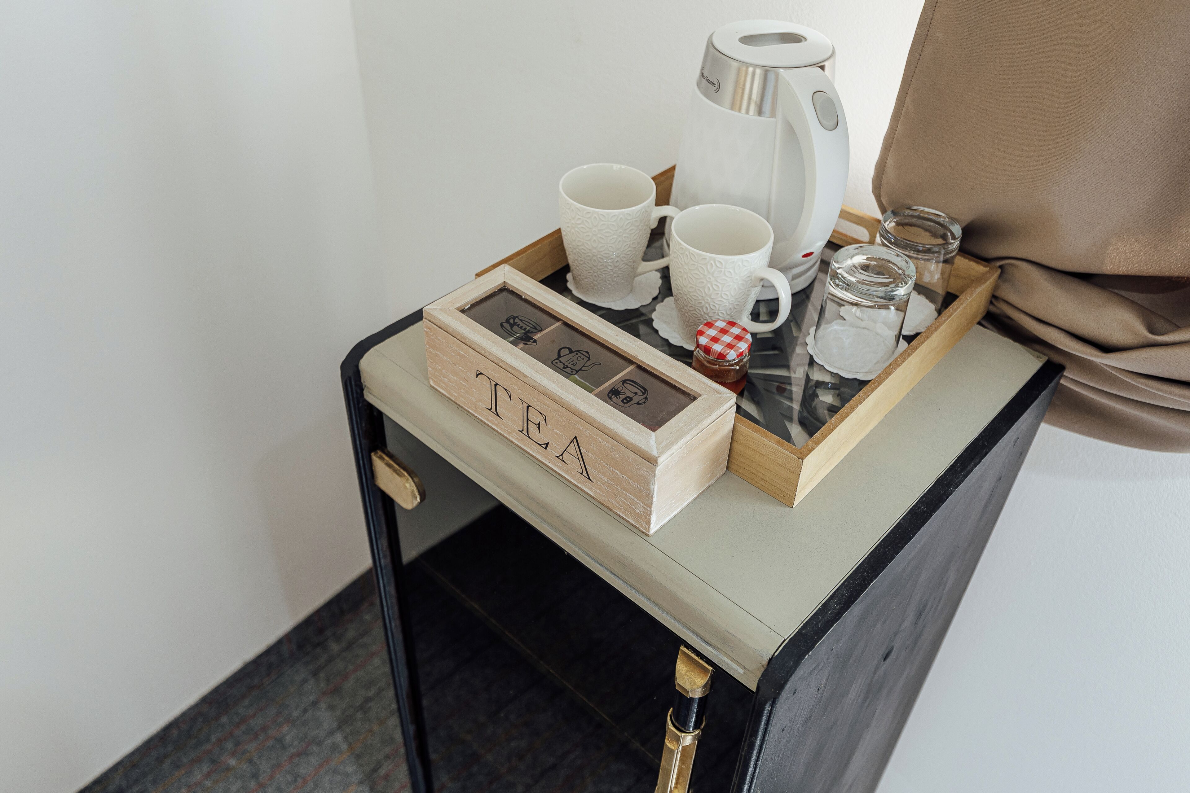 A small table with a tray holding a coffee maker, two cups, a jar, and a box labeled 'TEA'.