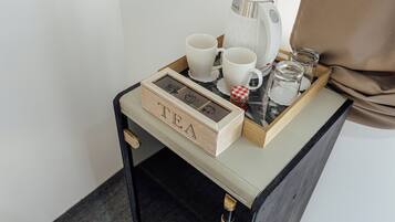 A small table with a tray holding a coffee maker, two cups, a jar, and a box labeled 'TEA'.