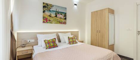 A hotel room with a bed, bedside table, nightstand, and a painting on the wall.
