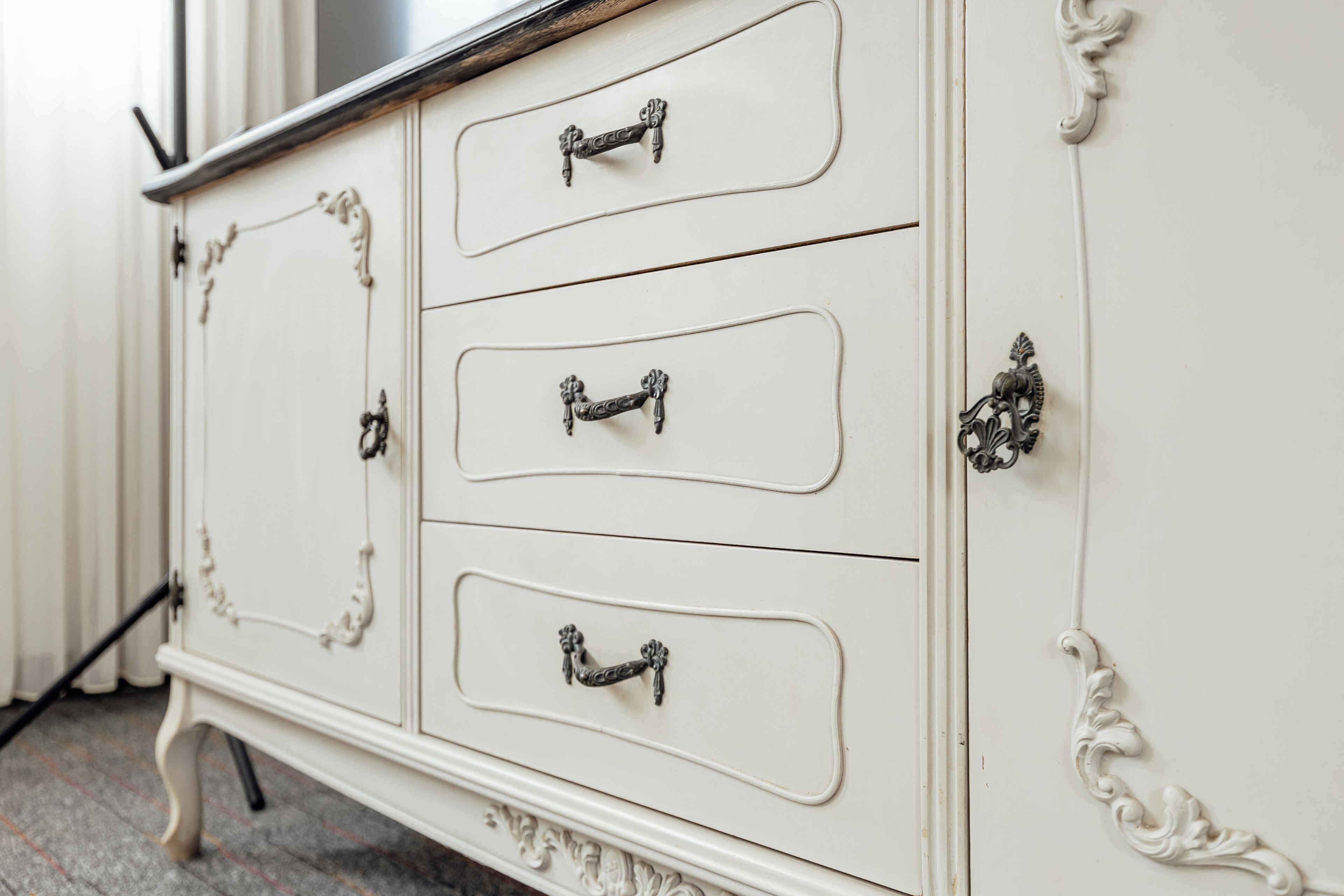 A white dresser with ornate handles and decorative moldings.