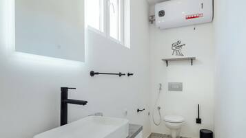 Un baño moderno con un lavamanos, inodoro y ducha blancos. Una ventana proporciona luz natural, y hay un perchero en la pared.