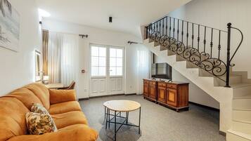 A living room with a sofa, a round table, a staircase with a decorative railing, and a TV cabinet.