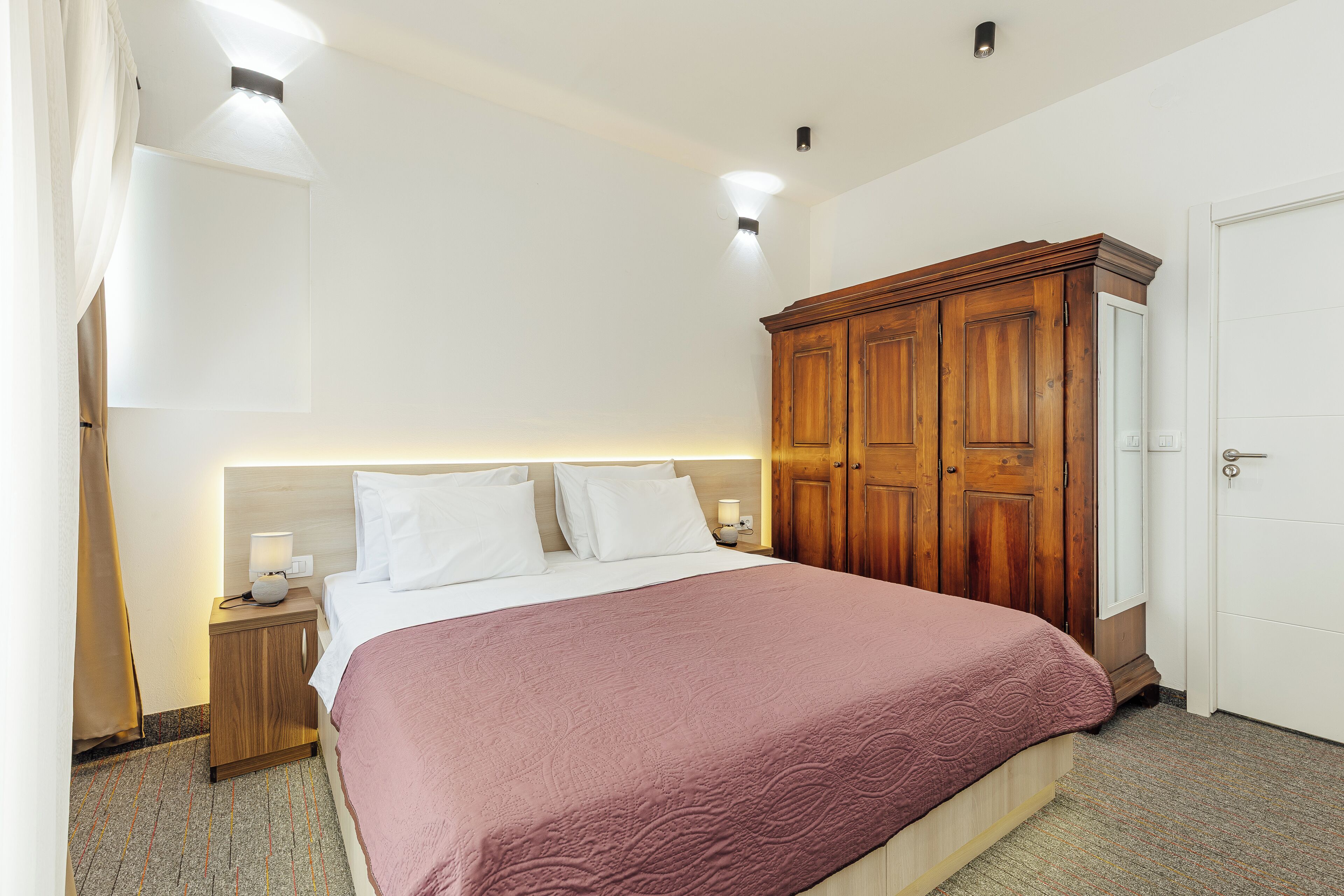 A hotel room with a bed, nightstands, a wardrobe, and a door.