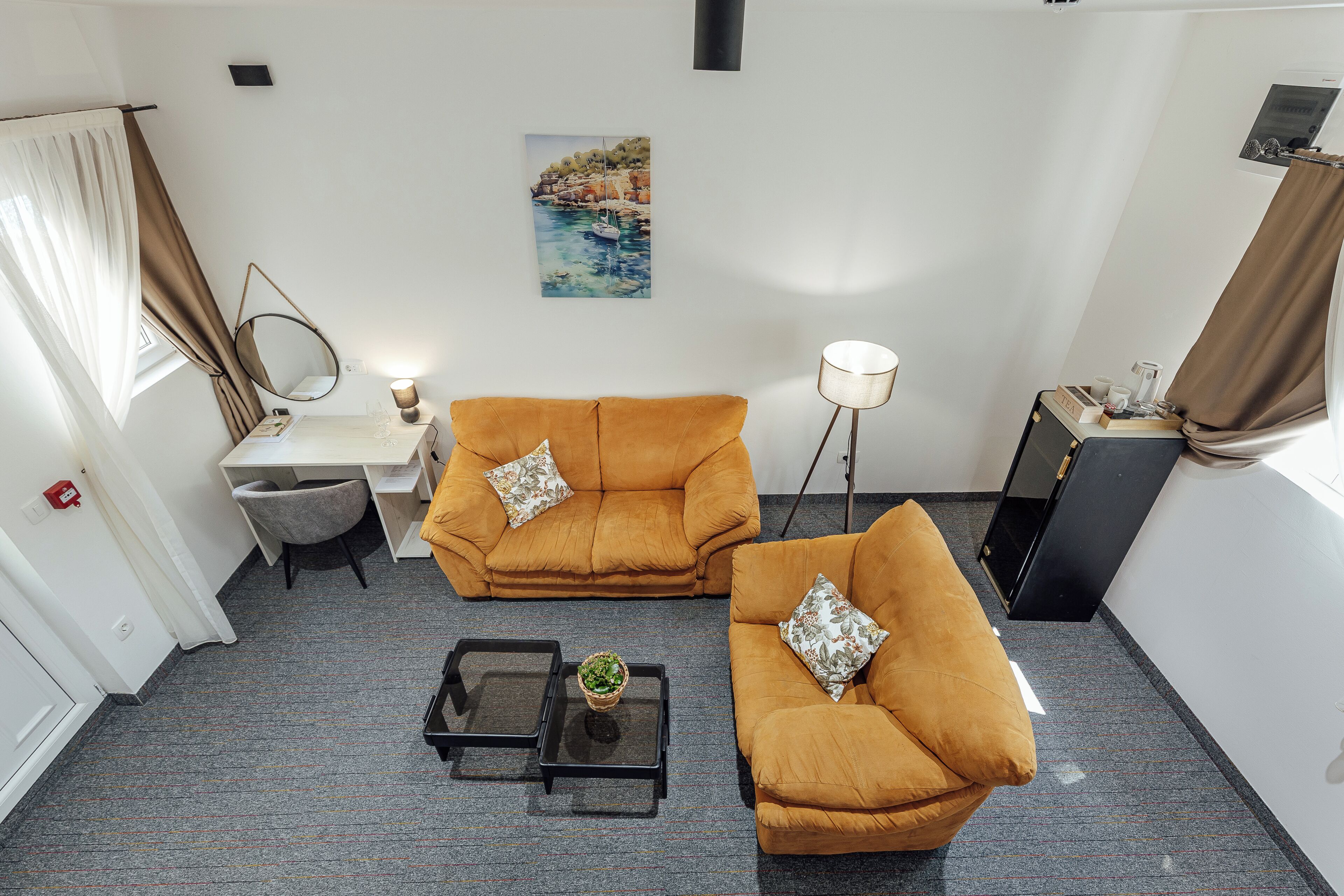 Une pièce avec deux canapés, une petite table, une lampe, un tableau et une fenêtre avec des rideaux.